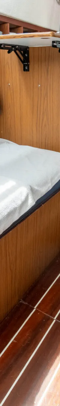 De foto toont het interieur van een boot met een slaapplaats, houten panelen, een koelkast en een trapje.