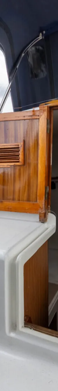 Een openstaande houten kajuitdeur met een ventilatierooster leidt naar het interieur van een boot, met uitzicht op water en…