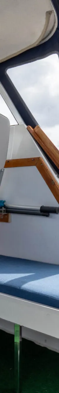 De foto toont het interieur van een boot met een stuurstoel, bankjes en een doorkijk naar de kajuit en het water.