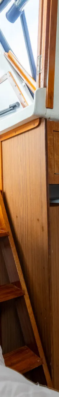 Een kajuit met een bed, een koelkast, houten kasten en een trapje naar een hoger gelegen gedeelte.
