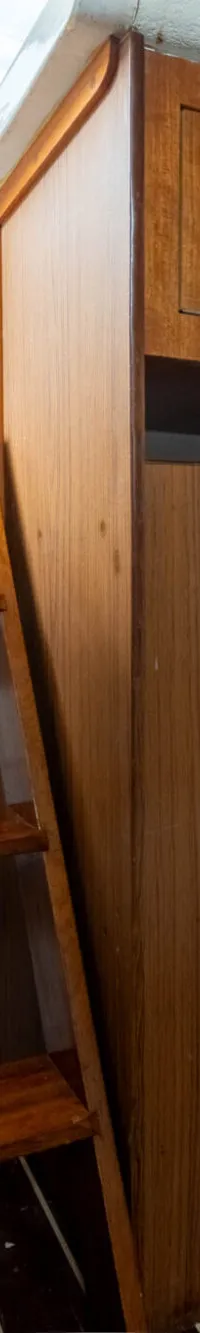 De foto toont een interieur van een boot met een bed, een houten trap, een witte koelkast en houten kasten.