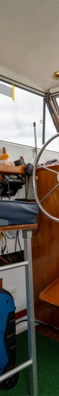 De foto toont het interieur van een boot met een stuurwiel, een blauwe stoel en een generator. — Amerglass Amerglass 32 OK AK