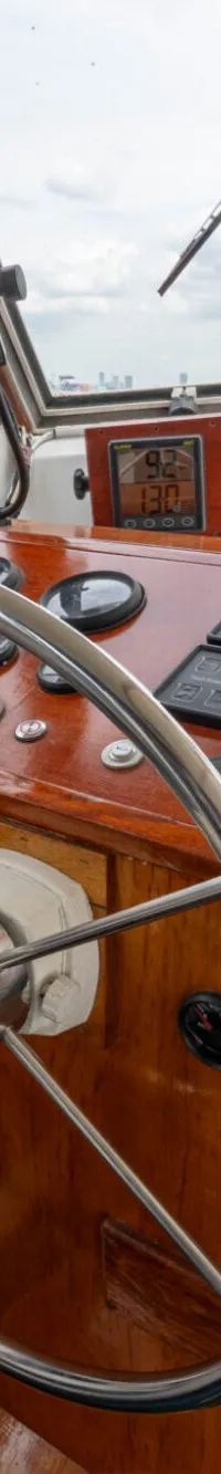 De foto toont het stuur en het dashboard van een boot, met uitzicht op water en bebouwing op de achtergrond.
