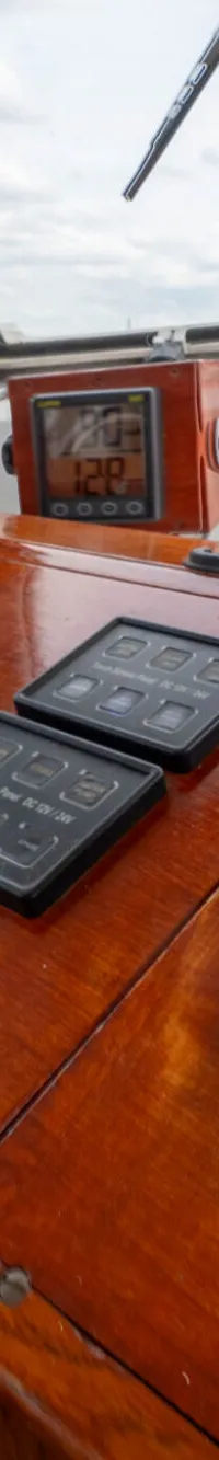Een houten dashboard met diverse meters, twee zwarte touchscreens, een stuurwiel en twee chromen hendels.