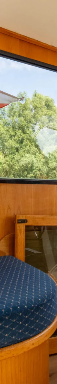 De kajuit toont een houten interieur met ramen, een blauw kussen, een vlag met "W V G" en een kompasroos op een deur.