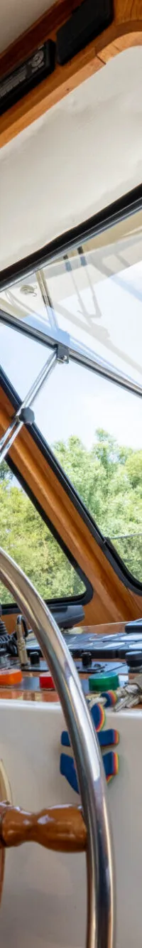 De stuurstand van een boot is zichtbaar, met een houten stuurwiel, bedieningspanelen en een kapiteinspop.