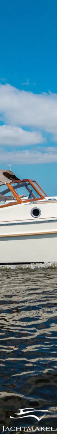 Een witte motorboot met een beige kap vaart over het water, met twee personen aan boord en een Nederlandse vlag achterop.