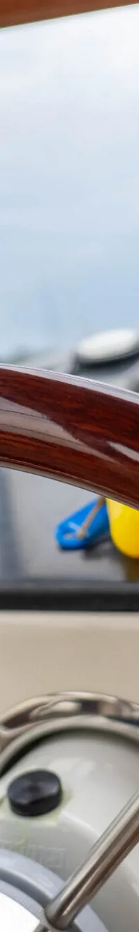 Een houten stuurwiel met metalen spaken is zichtbaar, met daarachter een dashboard met bedieningselementen en een raam.