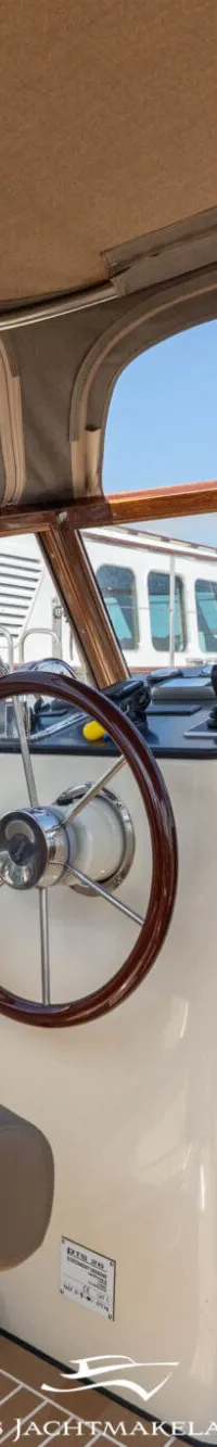 De foto toont het interieur van een boot met een stuurwiel, een beige stoel en een open kajuit met beddengoed. — PTS PTS 26