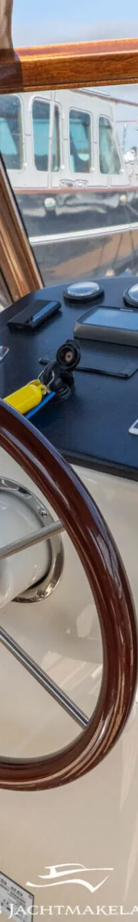 Een stuurwiel met houten rand en metalen spaken is zichtbaar, met daarachter een dashboard met diverse meters en een tablet.