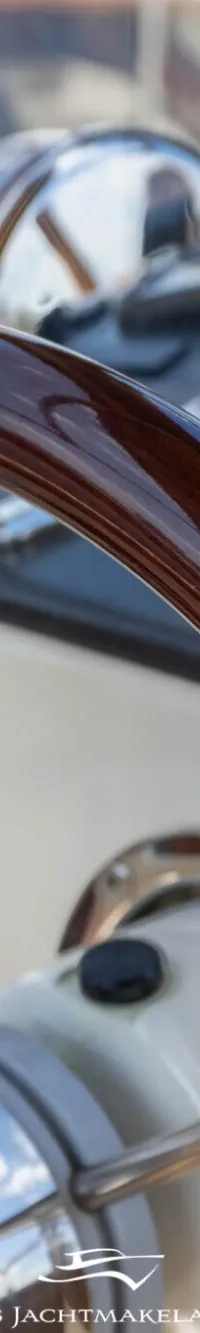 Een close-up van een glanzend bruin houten stuurwiel met chromen spaken en een dashboard met navigatieapparatuur.