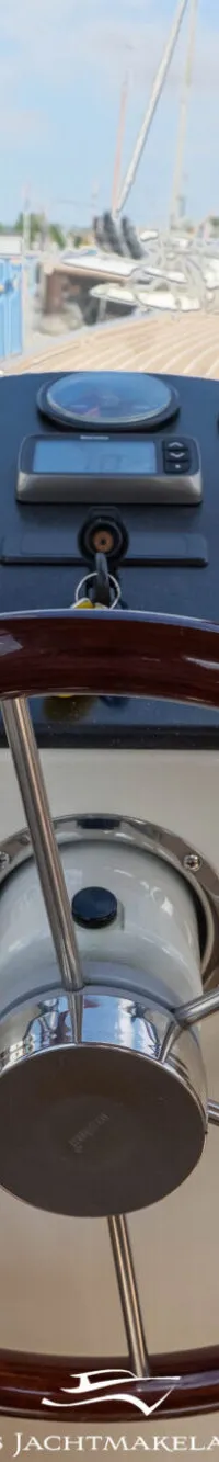 Een houten stuurwiel en een dashboard met diverse meters en een tablet zijn zichtbaar in de cockpit van een boot.