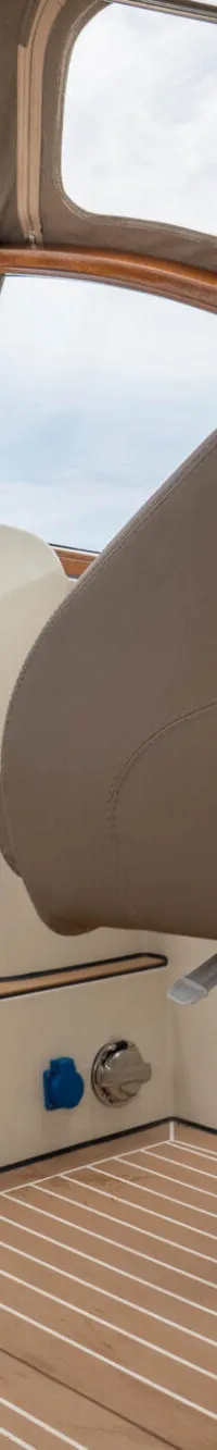 De foto toont het interieur van een boot met een beige stuurstoel, een houten vloer en een open doorgang naar een kajuit.
