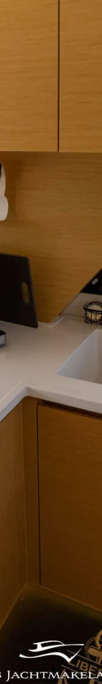 Een bootkeuken met een kookplaat, spoelbak, koffiezetapparaat, houten kasten en een papieren handdoekhouder.