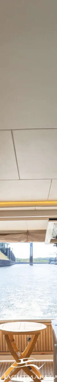 Een interieur van een boot met een keukenblok, houten kasten, een raam met uitzicht op water en een plafond met verlichting.
