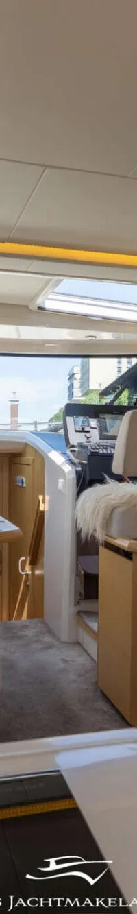 Een interieur van een boot met een keukenblok, zitgedeelte, stuurstand en ramen met uitzicht op water en bebouwing.