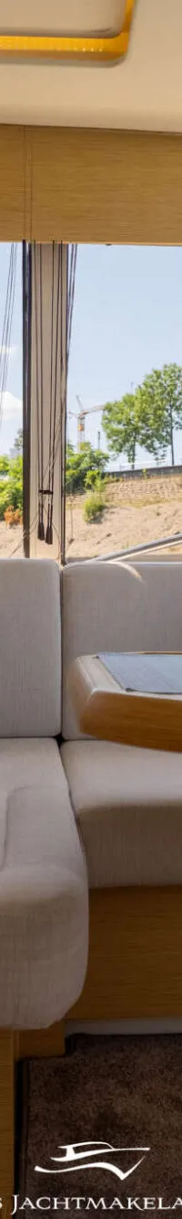 Een interieur van een boot met een U-vormige bank, een houten tafel en grote ramen met uitzicht op groen en gebouwen.