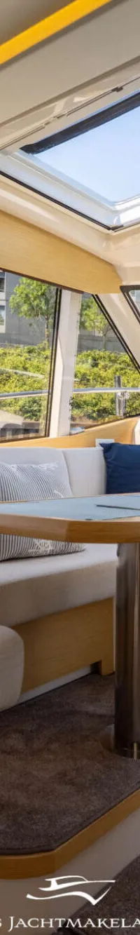 De foto toont een interieur van een boot met een zithoek, een tafel, ramen met uitzicht en een dakraam.