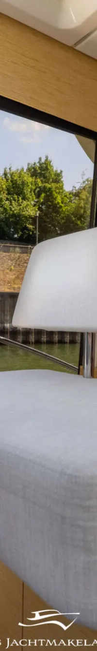 Een interieur van een boot met een stuurwiel, een witte bank en uitzicht op water en groen. — Greenline Greenline 39