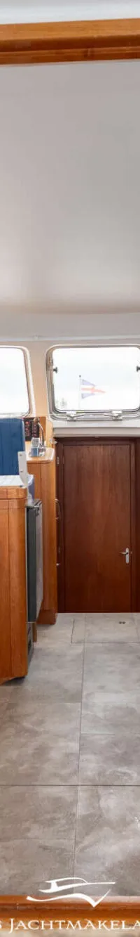 De foto toont het interieur van een boot met een kombuis aan de linkerkant en een zithoek aan de rechterkant.
