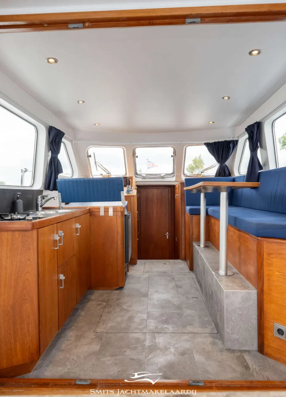 De foto toont het interieur van een boot met een kombuis aan de linkerkant en een zithoek aan de rechterkant.