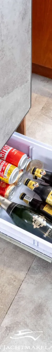 Een open koellade met blikjes frisdrank, bierflesjes en een fles mousserende wijn, omringd door houten panelen en een…