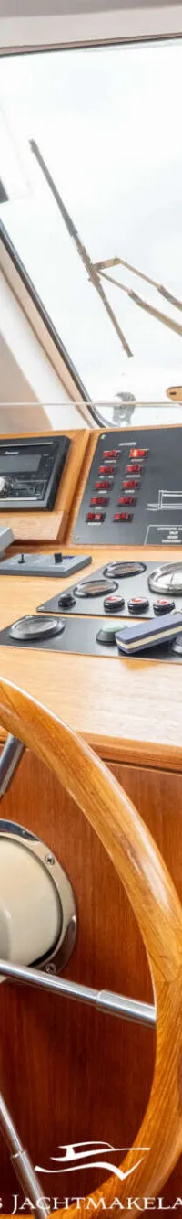 De foto toont het stuurhuis van een boot met een houten stuurwiel, diverse navigatie-instrumenten en een blauwe bank.