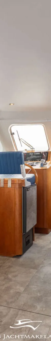 De foto toont het interieur van een boot met een kombuis, zithoek, stuurstand en ramen.
