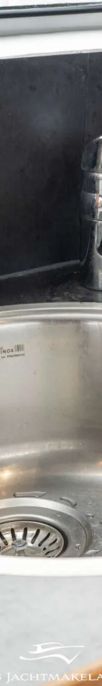 Een roestvrijstalen spoelbak met kraan en een zeepdispenser op een donker aanrechtblad.