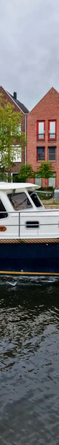 Een blauw-witte motorboot met de naam "Kimberley" vaart op een kanaal langs huizen en bomen. — Brandsma Brandsma 11.00 OK SP