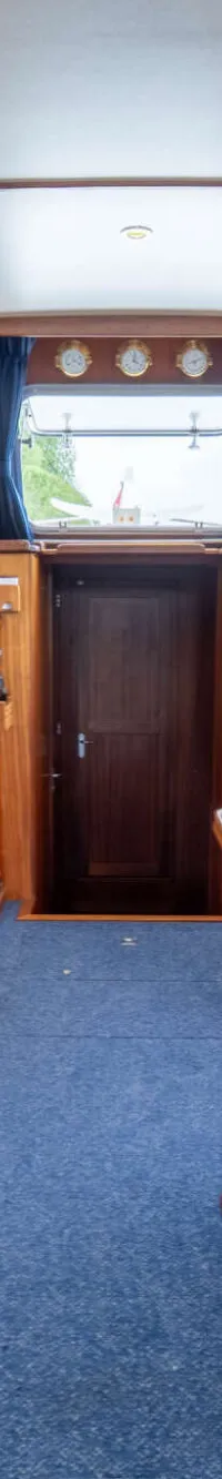De foto toont het interieur van een boot met houten lambrisering, blauwe bekleding en een stuurstand.