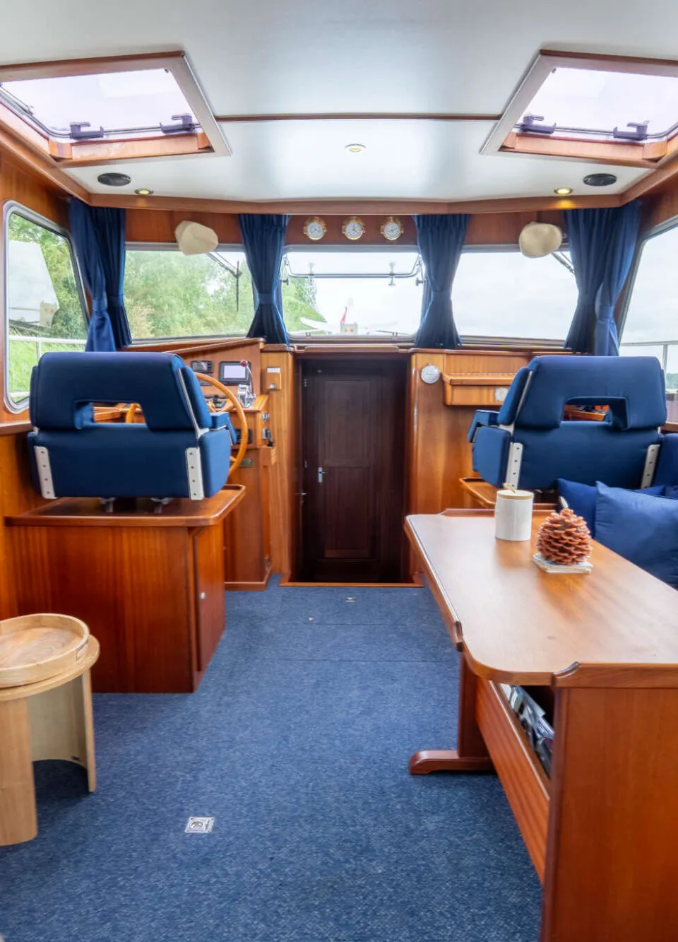 De foto toont het interieur van een boot met houten lambrisering, blauwe bekleding en een stuurstand.