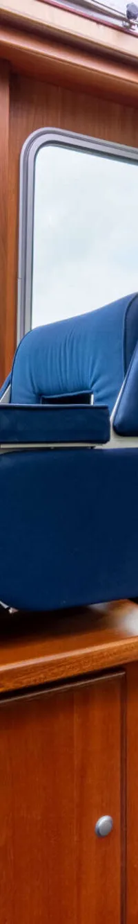 Het interieur van een boot met houten wanden, blauwe bekleding, een tafel en ramen met uitzicht naar buiten.