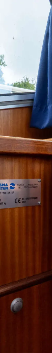 Een houten stuurwiel met chromen details, een blauwe stoffen zitting en een typeplaatje van Brandsma Jachten.