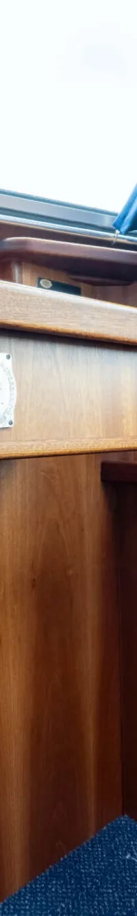 Een interieur van een boot met houten wanden, een blauw gordijn en drie portofoons op een plank.