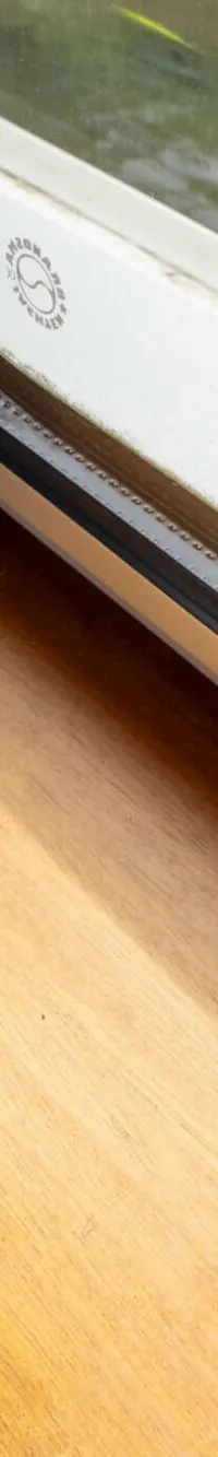Een houten oppervlak met een blauw gordijn en een raam waardoor water met planten zichtbaar is.