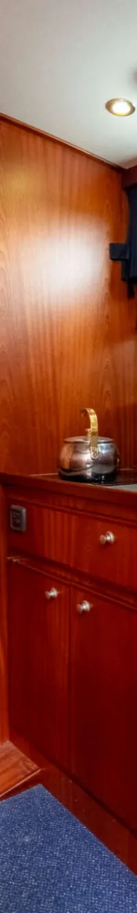Een houten kajuit met een kombuis, een deur, een raam en een blauw tapijt op de vloer. — Brandsma Brandsma 11.00 OK SP