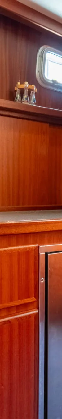 De foto toont een houten scheepskeuken met een magnetron, waterkoker, gootsteen, kraan, koffiezetapparaat en een koelkast.