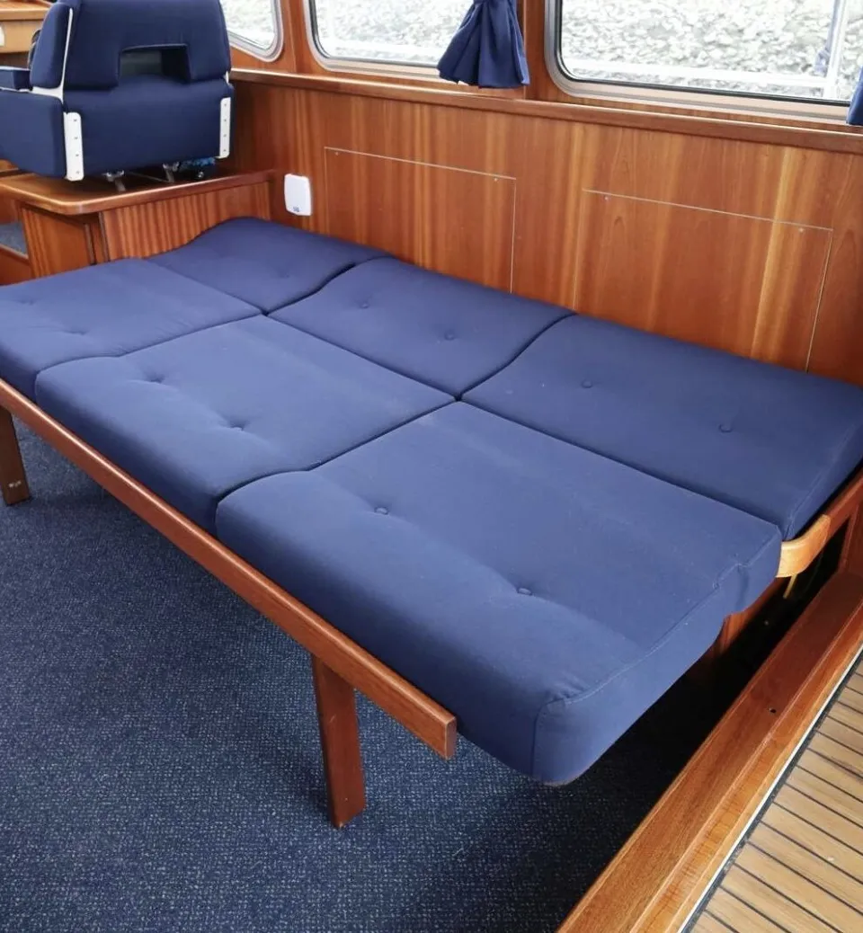 De foto toont het interieur van een boot met een blauw tapijt, houten lambrisering, blauwe banken, een houten tafel en…