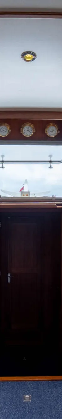 De foto toont het interieur van een boot met een houten stuurwiel, blauwe stoelen en houten afwerking.