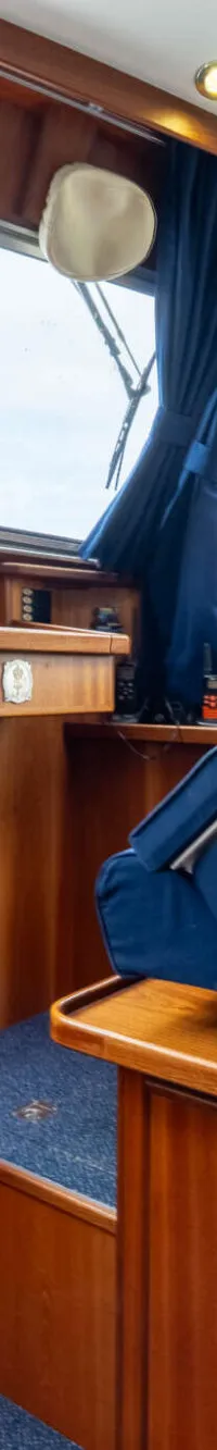 Een interieur van een boot met houten wanden, blauwe bekleding en gordijnen, en ramen die uitzicht bieden op groen.