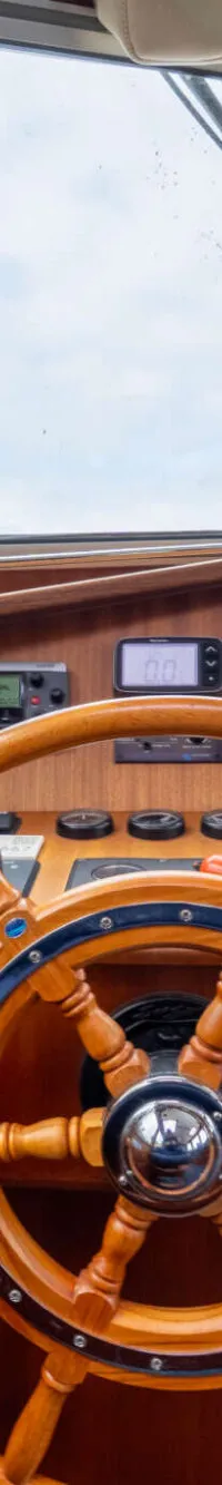 De foto toont het interieur van een stuurhut met een houten stuurwiel, diverse navigatie-instrumenten en ramen met blauwe…