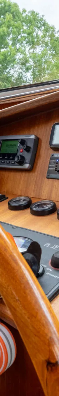 Een houten stuurwiel en dashboard met diverse meters, een Garmin-scherm en een chromen gashendel zijn zichtbaar.