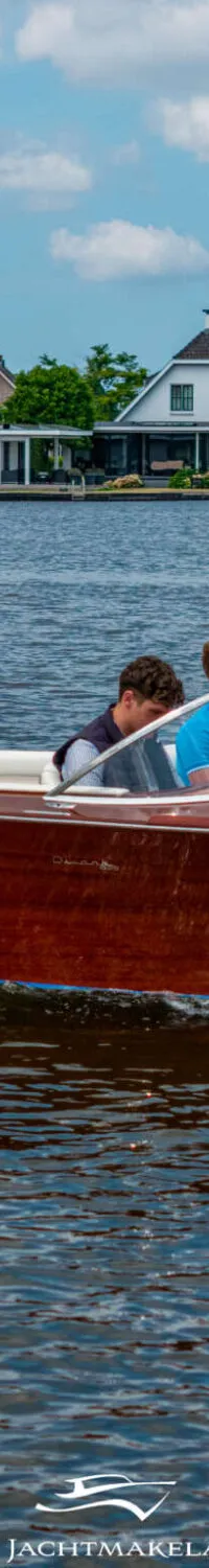 Een houten speedboot met twee mannen aan boord vaart over het water, met huizen op de achtergrond. — Divank Divank Uscire 635