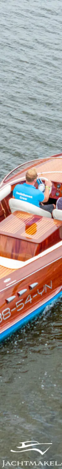 Een houten motorboot met twee personen vaart over het water, met registratienummer 38-54-YN op de zijkant.