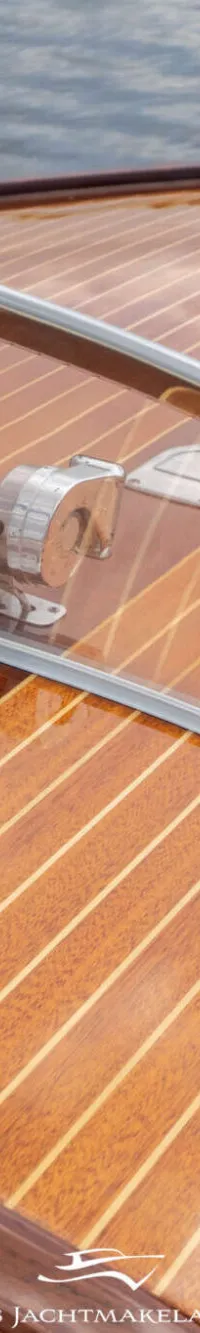 Een detailfoto van een houten bootdek met een transparante windscherm en een deel van het dashboard.