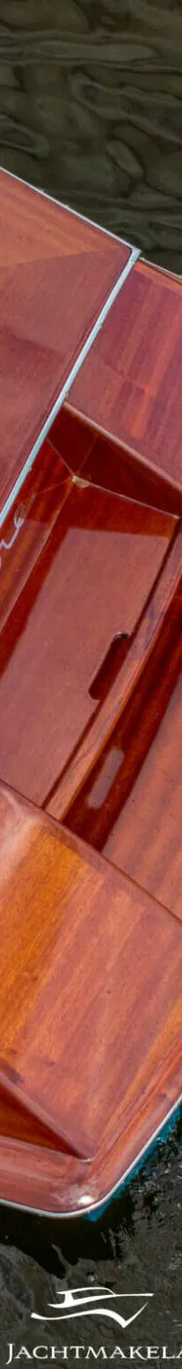 Een bovenaanzicht van de achtersteven van een houten boot met een wit zitkussen en een naam op de zijkant.