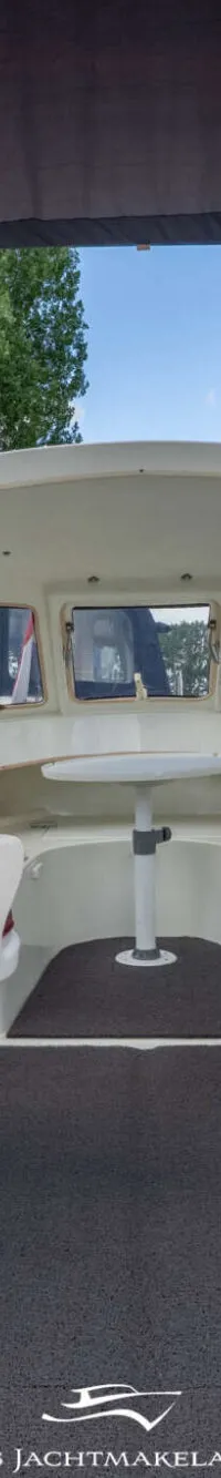 De foto toont het interieur van een boot met twee witte stoelen, een stuurwiel en een kleine tafel.