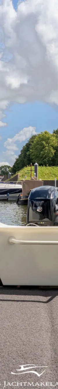 De foto toont de achterkant van een boot met een buitenboordmotor, een grijze vloerbedekking en twee stoelen.