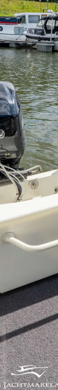 De foto toont de achterkant van een boot met een buitenboordmotor, een grijze vloerbedekking en een brandstoftank.